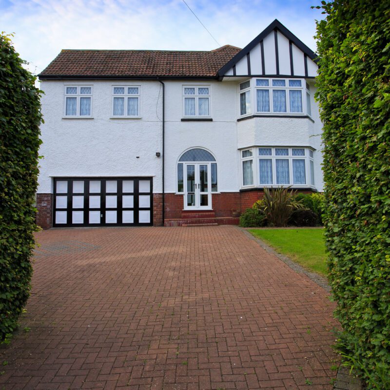 1930s white and black detached home with a bay window and large block paved driveway, in Bristol, England